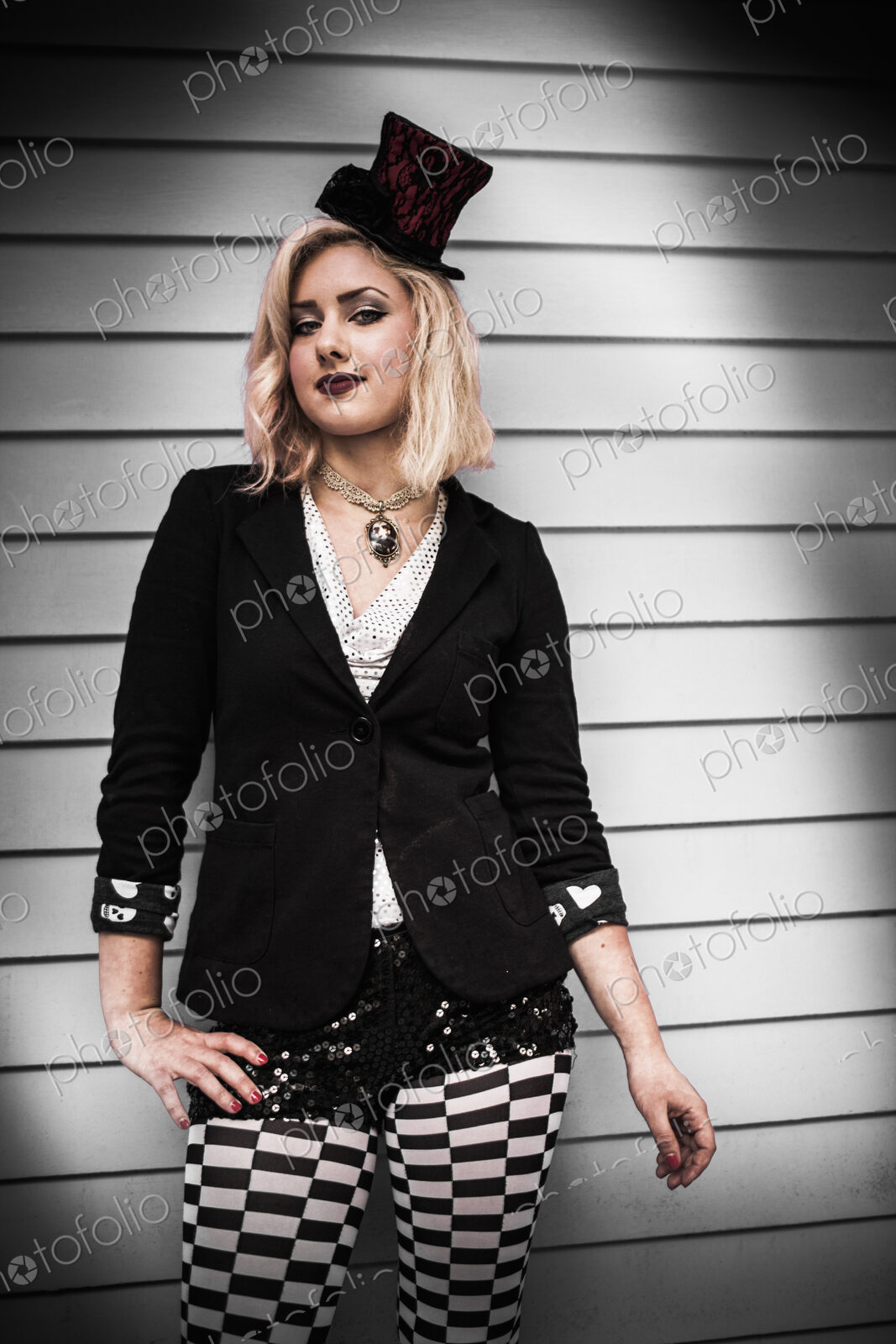 A young woman wearing a black tophat perched on the side of her head, and a black…