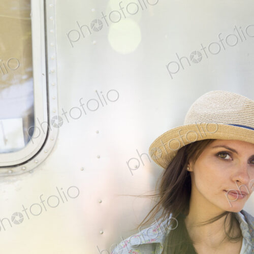 A young woman wearing a hat sitting in the shade of a silver coloured trailer. A young woman wearing a hat sitting in the shade of a silver coloured trailer.