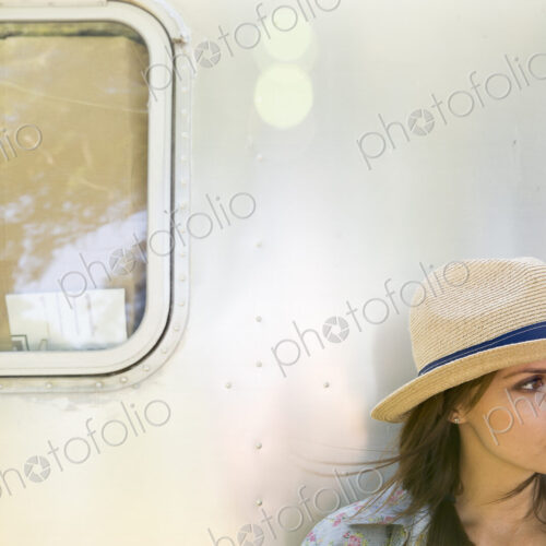 A young woman wearing a hat sitting in the shade of a silver trailer. A young woman wearing a hat sitting in the shade of a silver trailer.