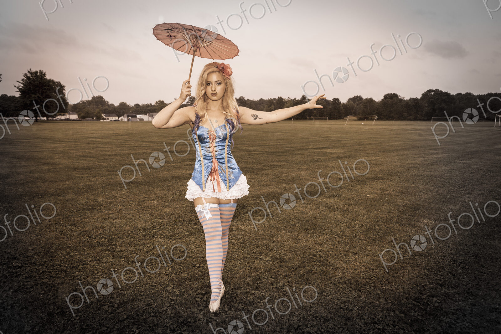 A young woman wearing a laced basque and frilly bloomers, striped stockings and…