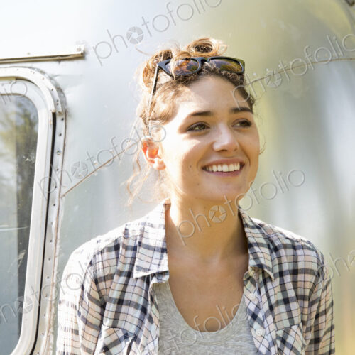 A young woman wearing sunglasses by a silver coloured trailer.