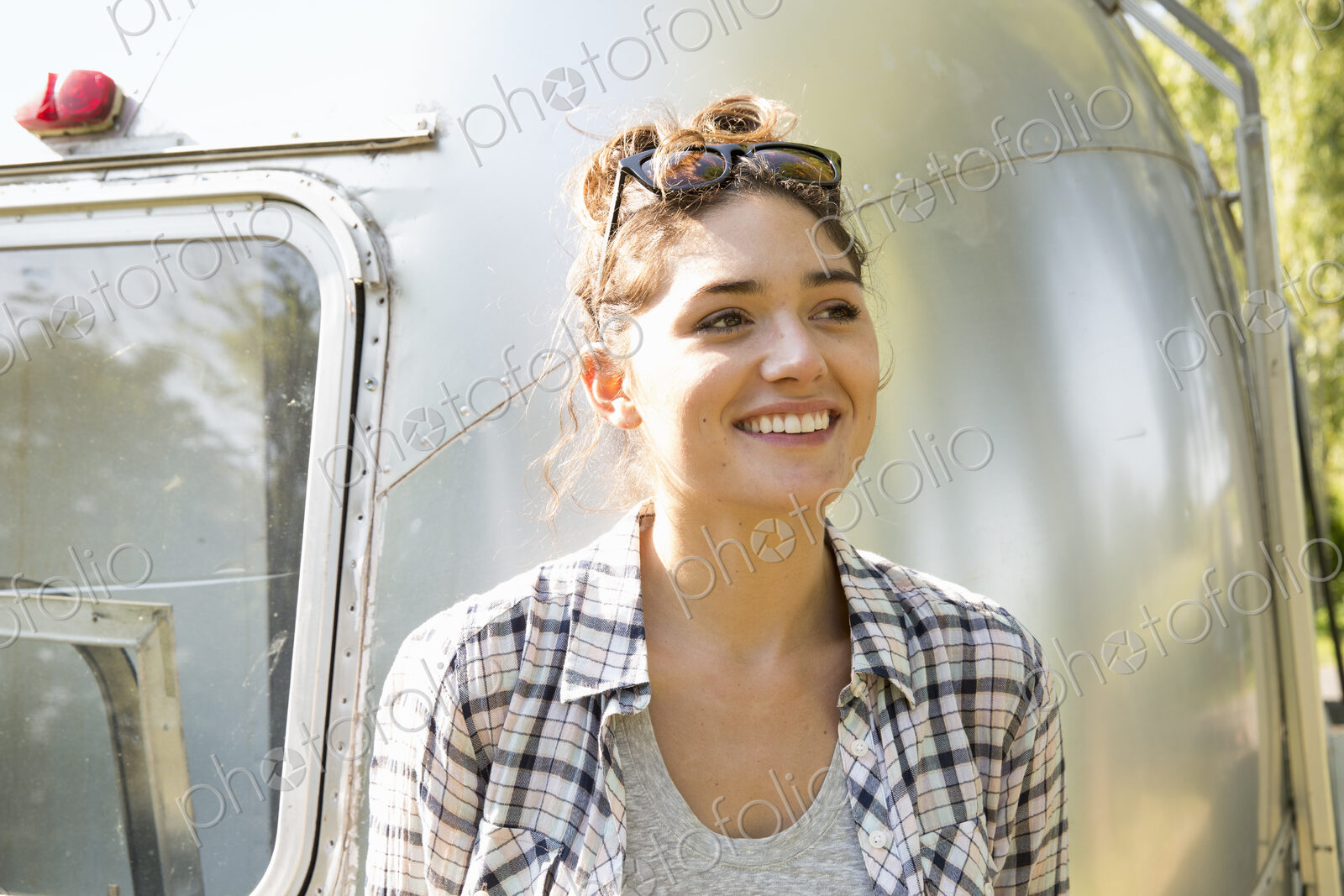 A young woman wearing sunglasses by a silver coloured trailer.