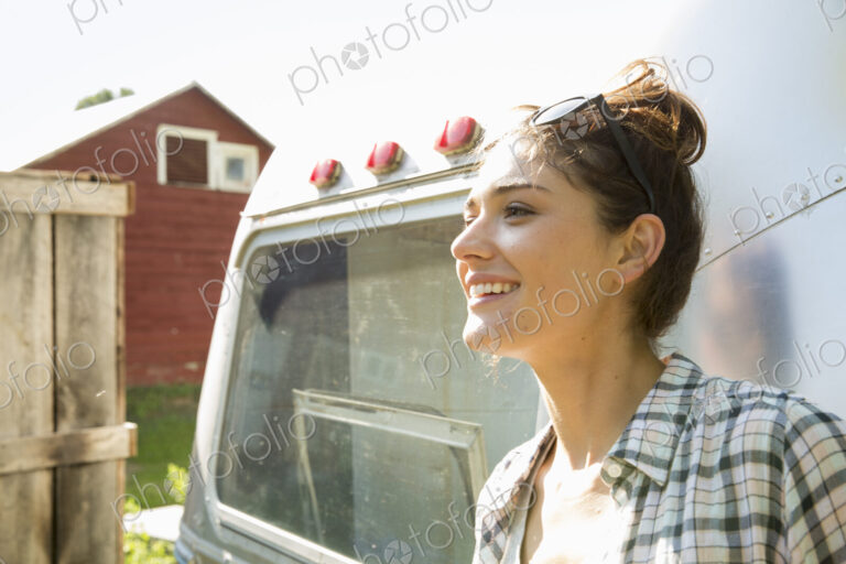 A young woman wearing sunglasses by a silver coloured trailer.
