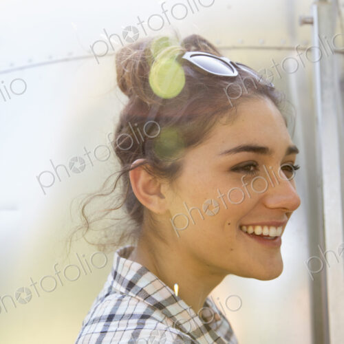 A young woman wearing sunglasses by a silver coloured trailer.