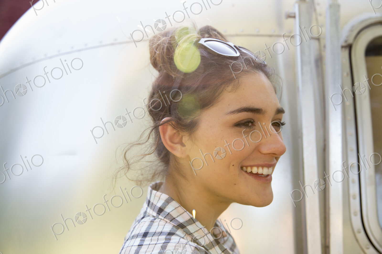 A young woman wearing sunglasses by a silver coloured trailer.