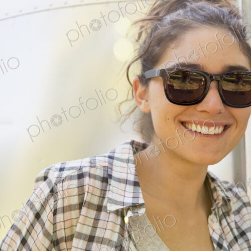 A young woman wearing sunglasses by a silver coloured trailer.