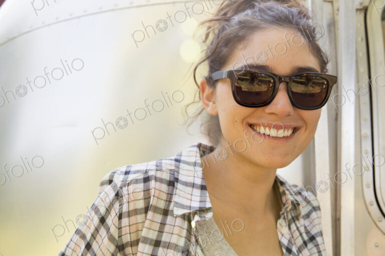A young woman wearing sunglasses by a silver coloured trailer.