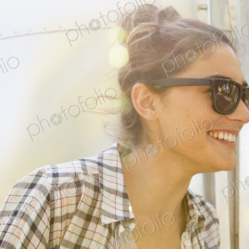 A young woman wearing sunglasses by a silver coloured trailer.