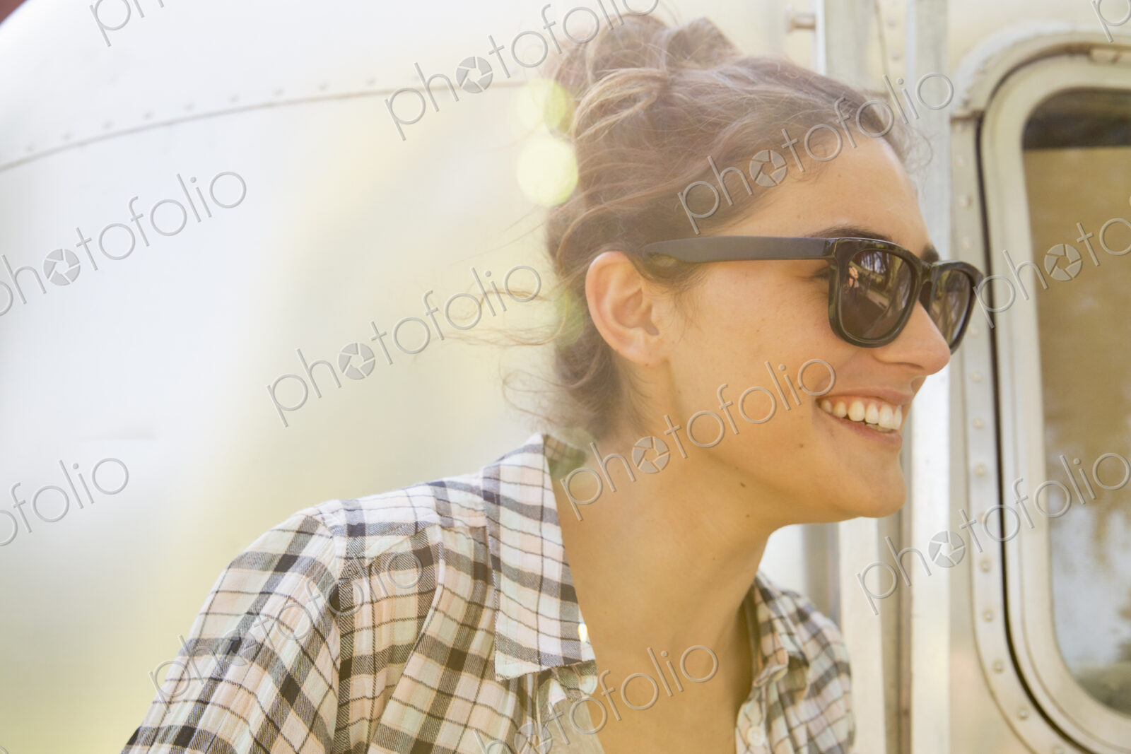 A young woman wearing sunglasses by a silver coloured trailer.