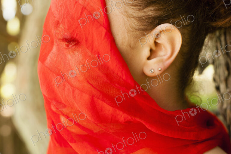 A young woman with a red seethrough sheer veil across her face.