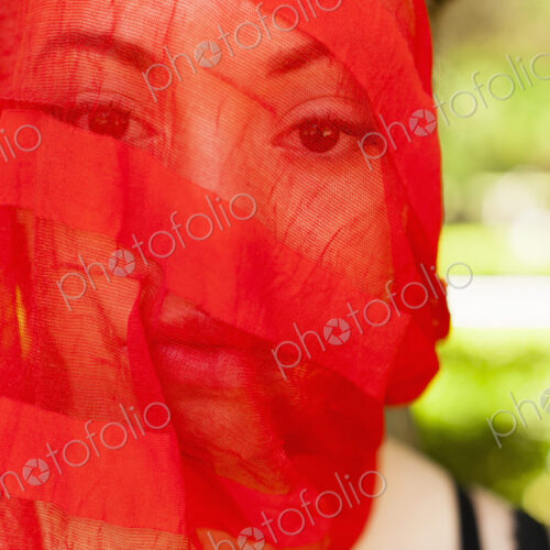 A young woman with a red seethrough sheer veil across her face. A young woman with a red seethrough sheer veil across her face.