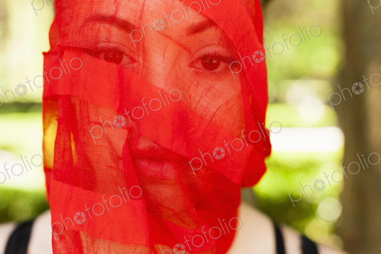 A young woman with a red seethrough sheer veil across her face.