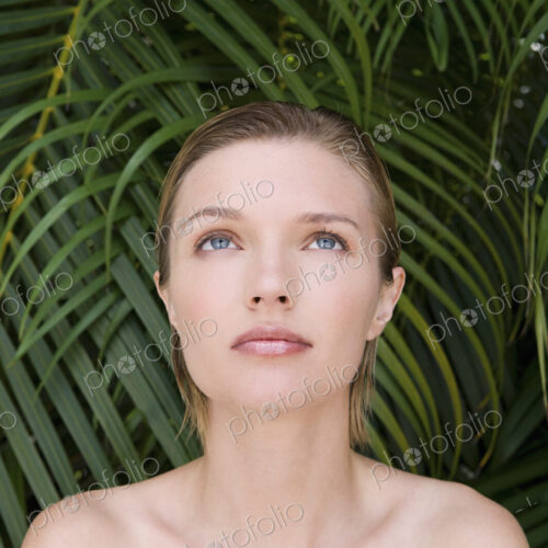 A young woman with bare shoulders, looking upwards. Tropical plants in the background. A young woman with bare shoulders, looking upwards. Tropical plants in the background.