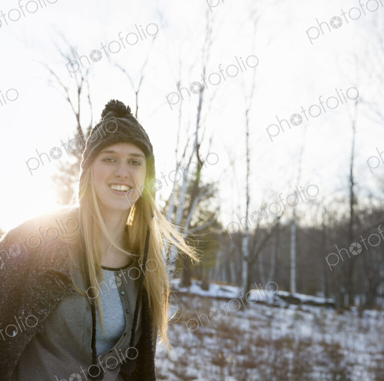 A young woman with blonde hair and a knitted woollen hat and coat. Outdoors on a…