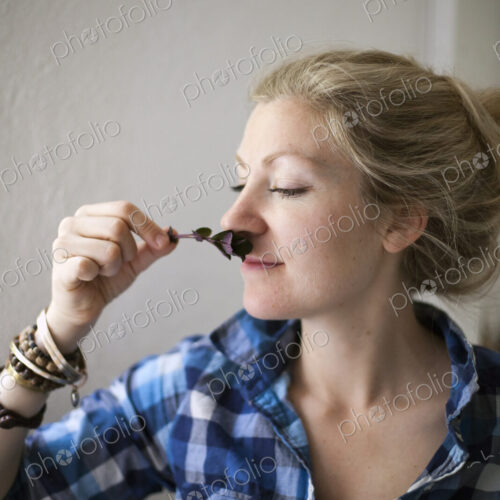 A young woman with blonde hair, holding a aromatic plant or herb flower to her nose…