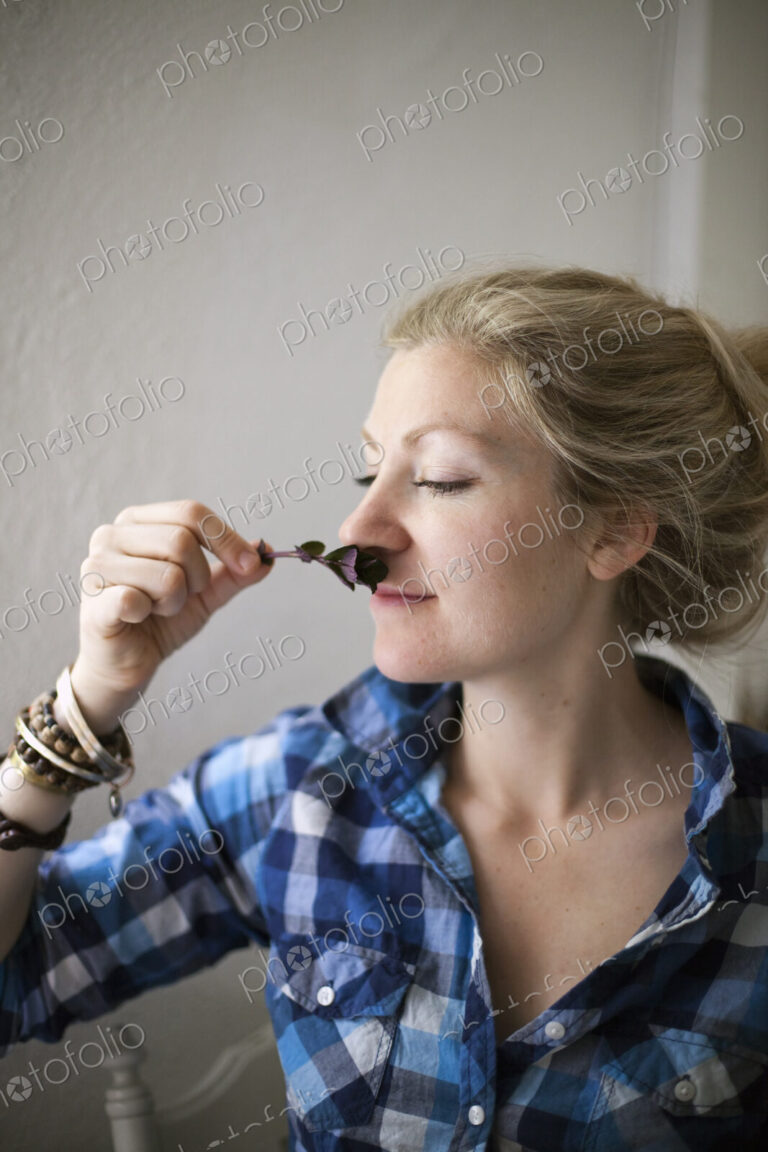 A young woman with blonde hair, holding a aromatic plant or herb flower to her nose…