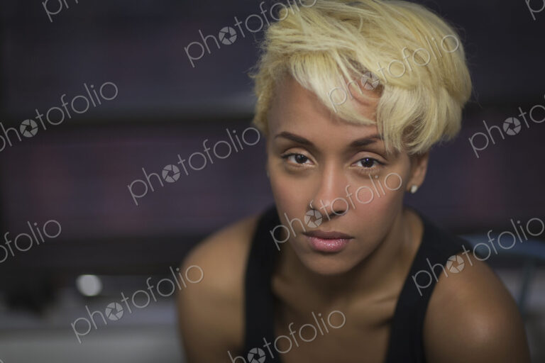 A young woman with blonde hair in a vest, looking at the camera.
