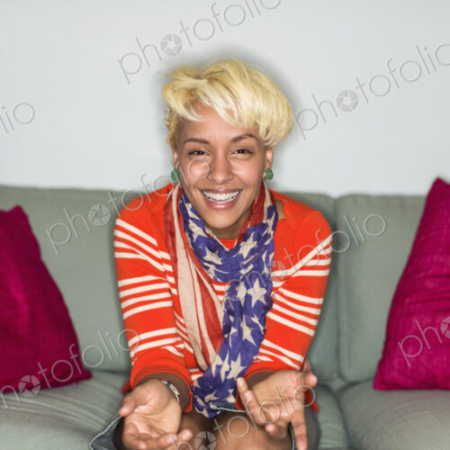 A young woman with blonde hair, seated on a sofa smiling.