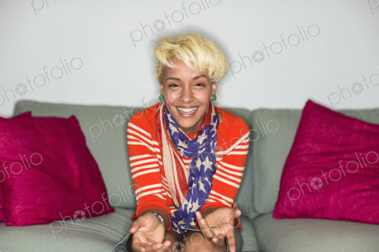 A young woman with blonde hair, seated on a sofa smiling.