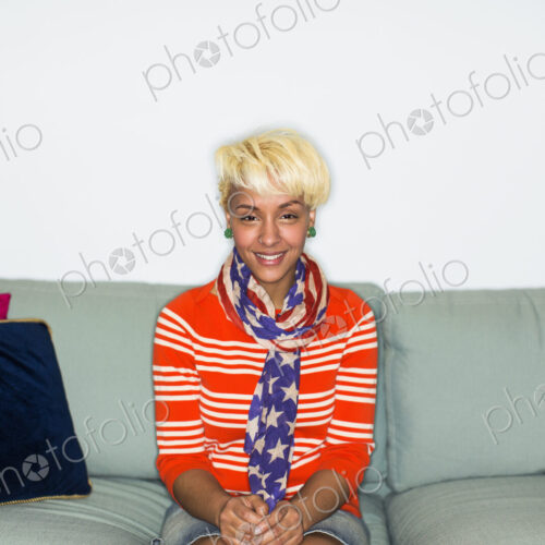 A young woman with blonde hair, seated on a sofa smiling.