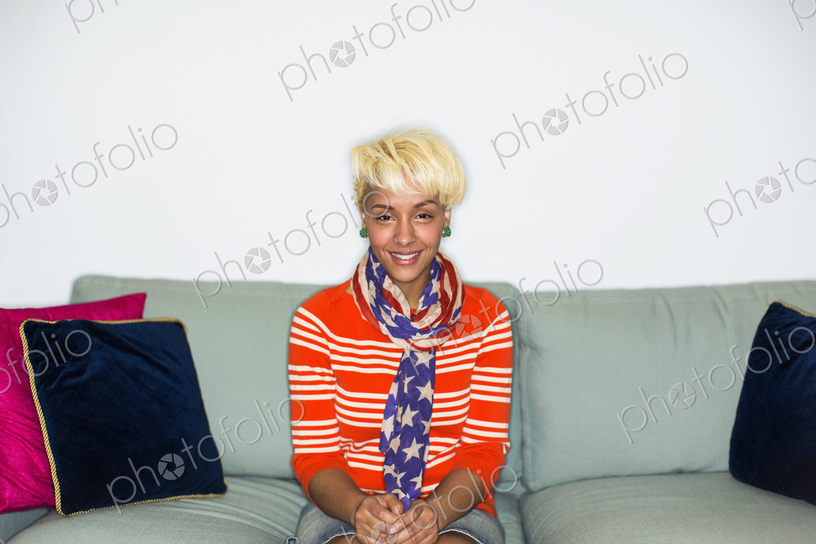 A young woman with blonde hair, seated on a sofa smiling.
