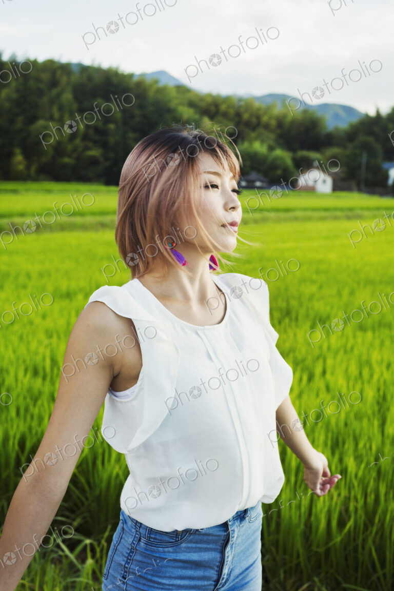 A young woman with hands outstretched, standing in rice paddy fields.