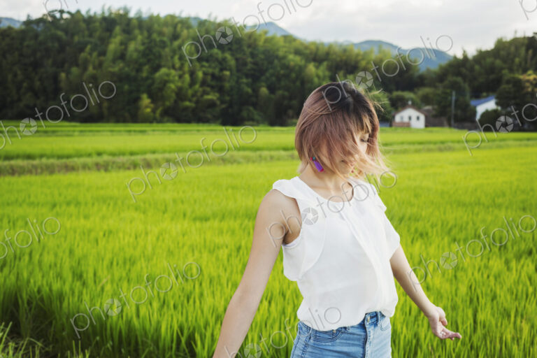 A young woman with hands outstretched, standing in rice paddy fields.