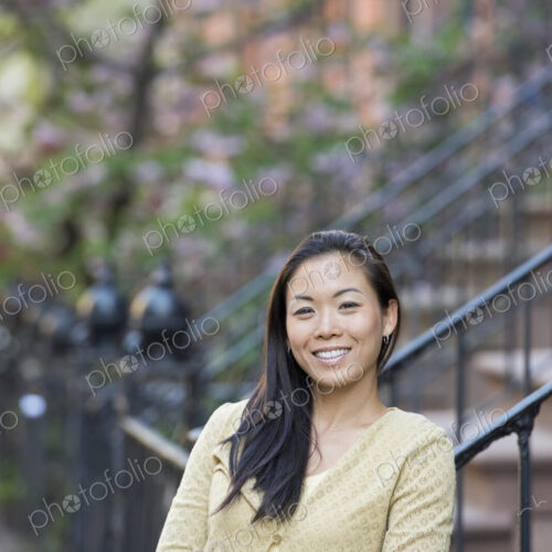 A young woman with long black hair, leaning on a railing at the bottom of a flight of…