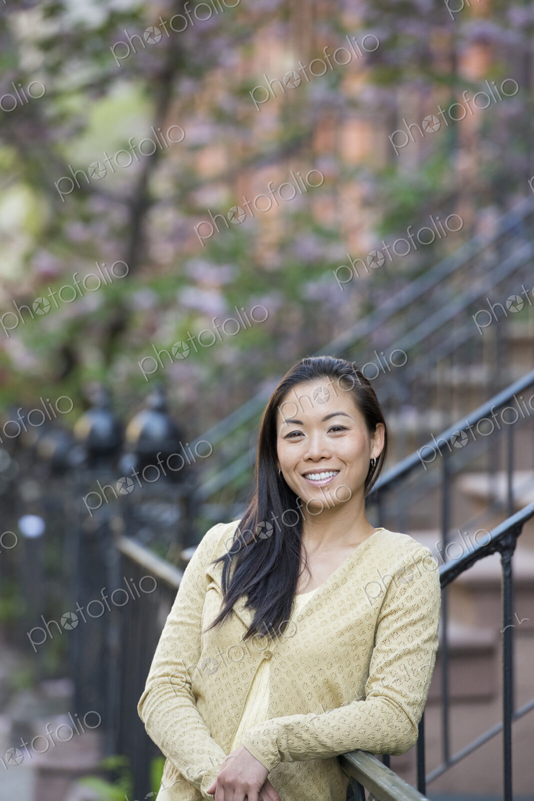 A young woman with long black hair, leaning on a railing at the bottom of a flight of…