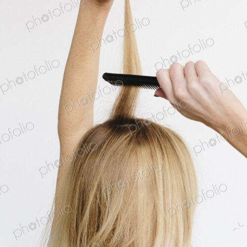A young woman with long blond wavy hair using a comb. Back view. A young woman with long blond wavy hair using a comb. Back view.