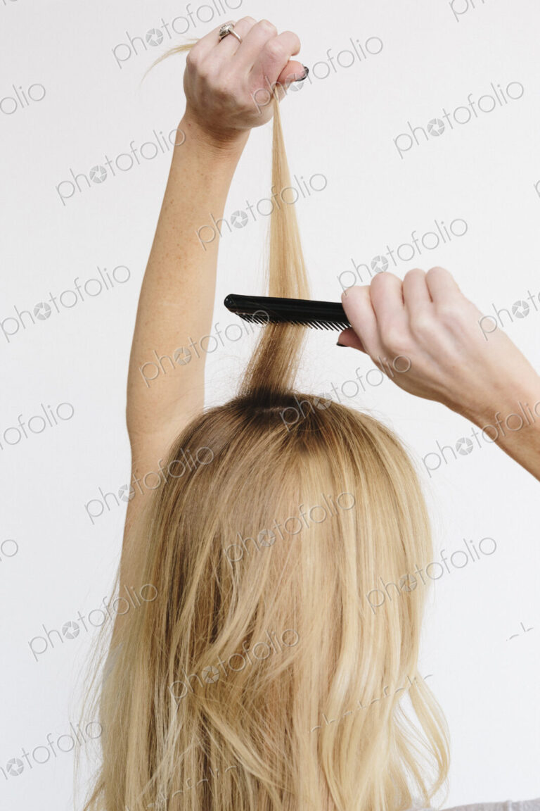 A young woman with long blond wavy hair using a comb. Back view.
