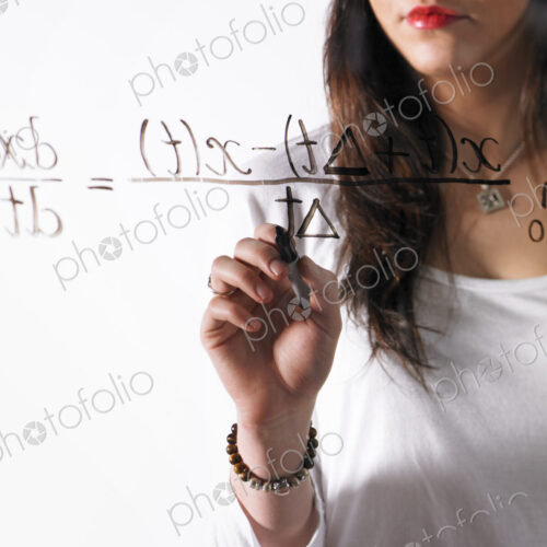A young woman writing a mathematical equation with black marker on a clear seethrough…