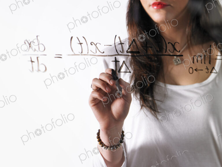 A young woman writing a mathematical equation with black marker on a clear seethrough…