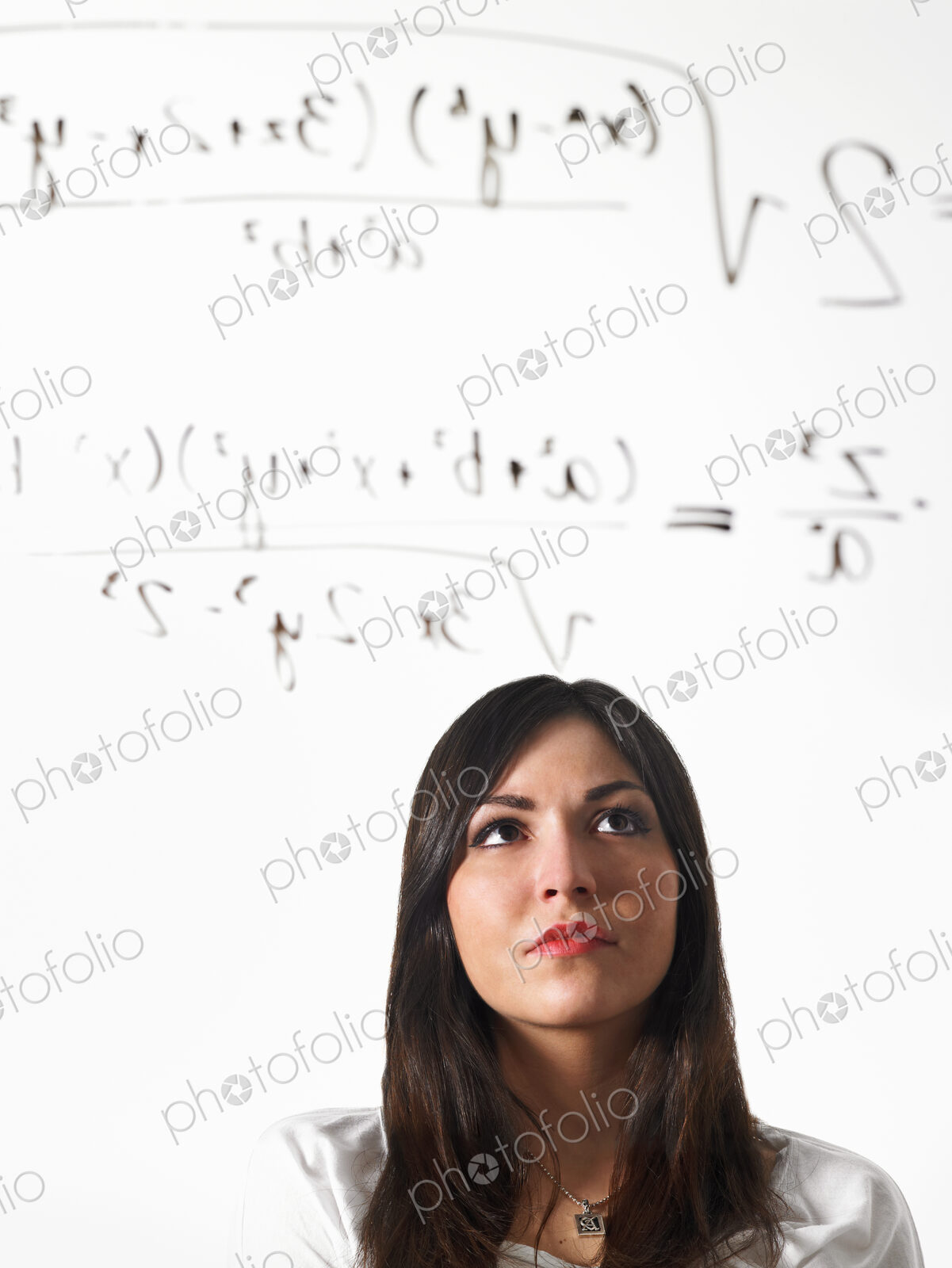 A young woman writing a mathematical equation with black marker on a clear seethrough…