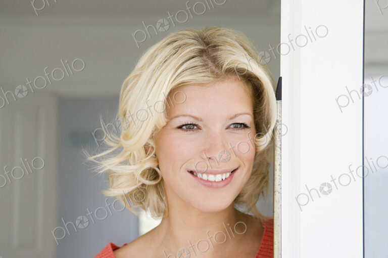 A young women with blonde hair smiling in a doorway.