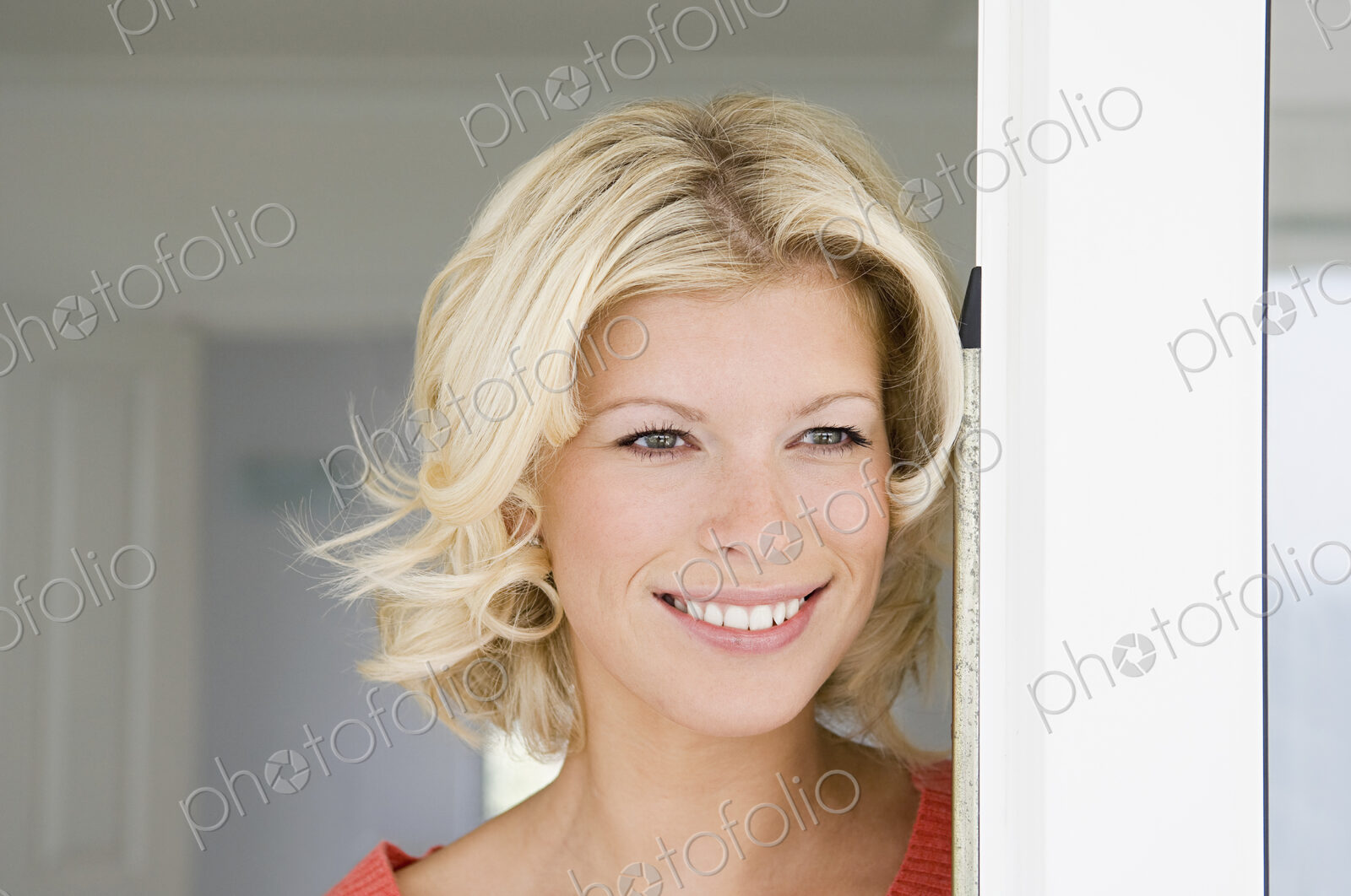 A young women with blonde hair smiling in a doorway.