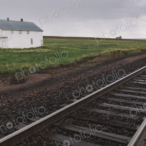 Abandoned farmhouse on prairie, train tracks in foreground, Saskatchewan, Canada.