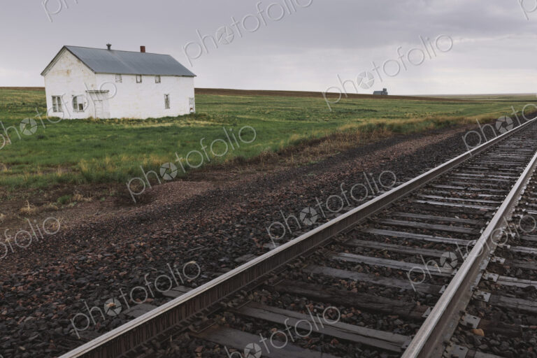 Abandoned farmhouse on prairie, train tracks in foreground, Saskatchewan, Canada.