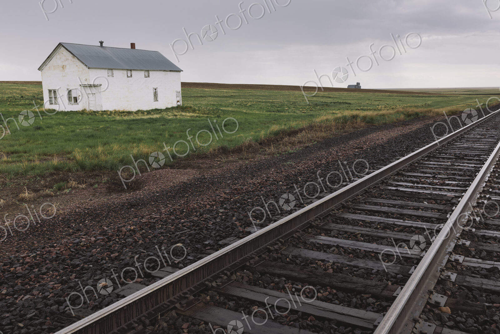 Abandoned farmhouse on prairie, train tracks in foreground, Saskatchewan, Canada.