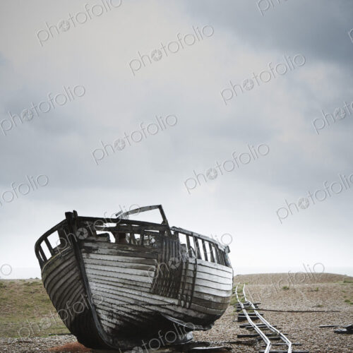 Abandoned wooden boat beached on the shingle by an old narrow gauge track.