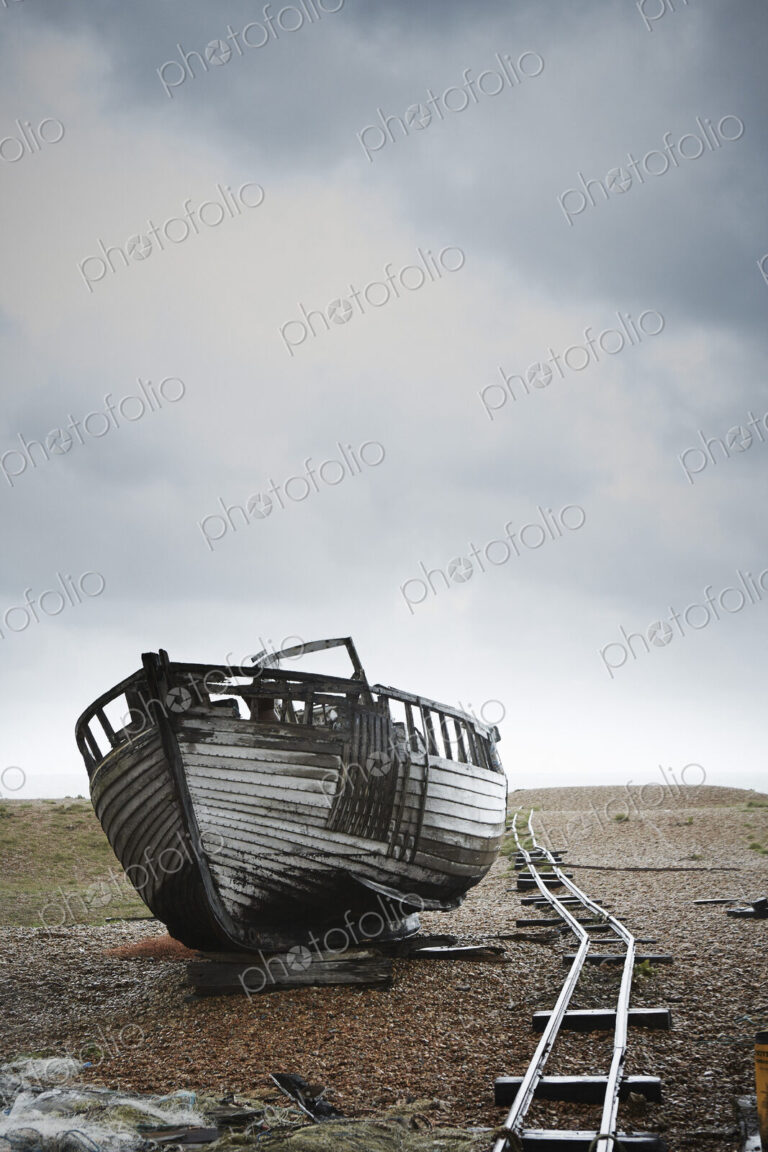 Abandoned wooden boat beached on the shingle by an old narrow gauge track.