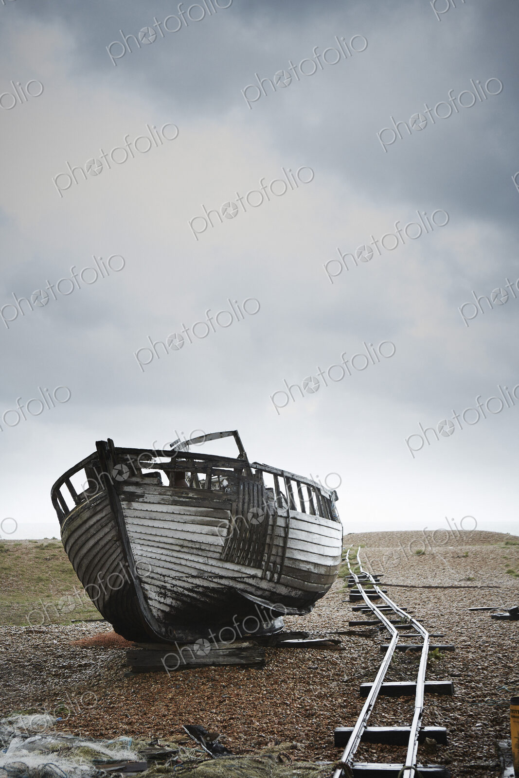 Abandoned wooden boat beached on the shingle by an old narrow gauge track.