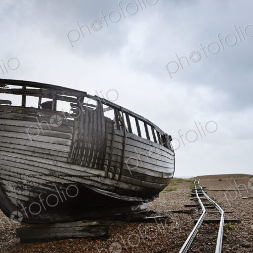 Abandoned wooden boat beached on the shingle near old narrow gauge rails.