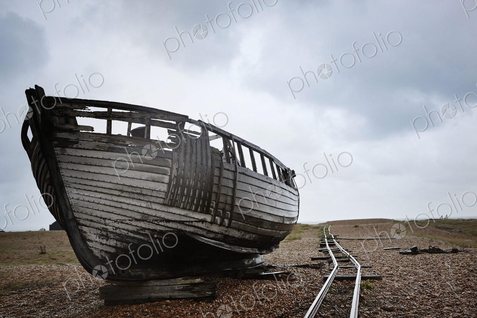 Abandoned wooden boat beached on the shingle near old narrow gauge rails.