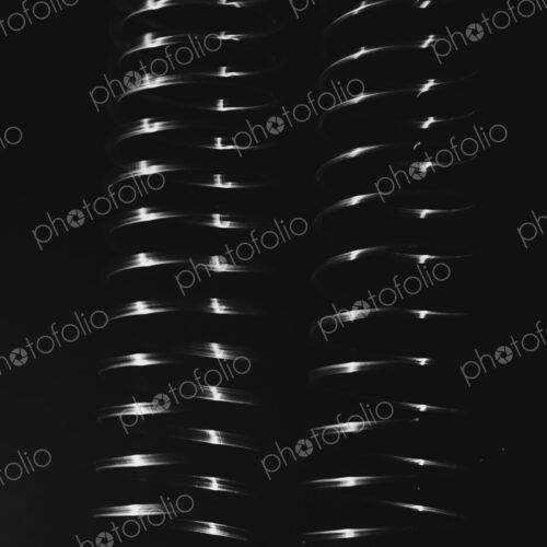 Abstract pattern, light shining on a length of fine wire wound around and stretched,…