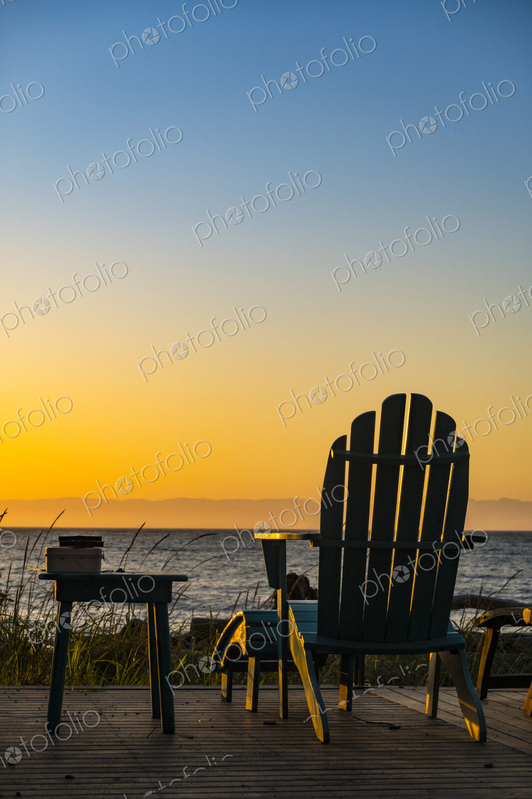 Adirondack chairs on the beach at sunset, an orange sunset glow on the horizon.