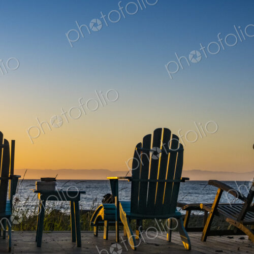 Adirondack chairs on the beach at sunset, an orange sunset glow on the horizon. Adirondack chairs on the beach at sunset, an orange sunset glow on the horizon.