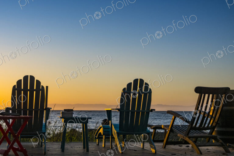 Adirondack chairs on the beach at sunset, an orange sunset glow on the horizon.