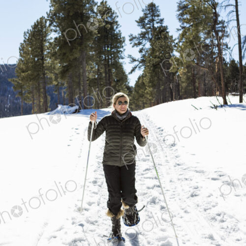 Adult woman wearing snow shoes with poles on a trail.