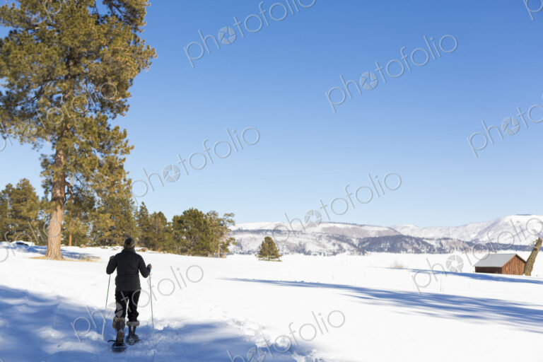 Adult woman wearing snow shoes with poles on a trail.